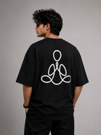 A man wearing a black oversized t-shirt with a white continuous line graphic on the back, shown from behind against a neutral gray studio background.