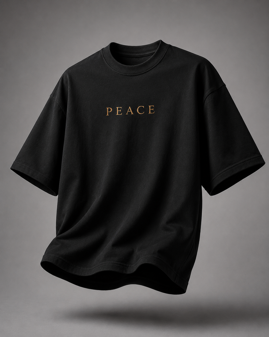 A black oversized short-sleeve t-shirt with the word 'PEACE' printed in gold across the chest, shown floating against a neutral gray background.