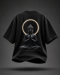 A black oversized short-sleeve T-shirt shown from the back, featuring a large graphic of a seated Buddha figure with hands in prayer, framed by a glowing circular halo. The shirt is centered on a dark gray gradient background with a soft shadow beneath it.