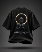 A black oversized short-sleeve T-shirt shown from the back, featuring a large graphic of a seated Buddha figure with hands in prayer, framed by a glowing circular halo. The shirt is centered on a dark gray gradient background with a soft shadow beneath it.