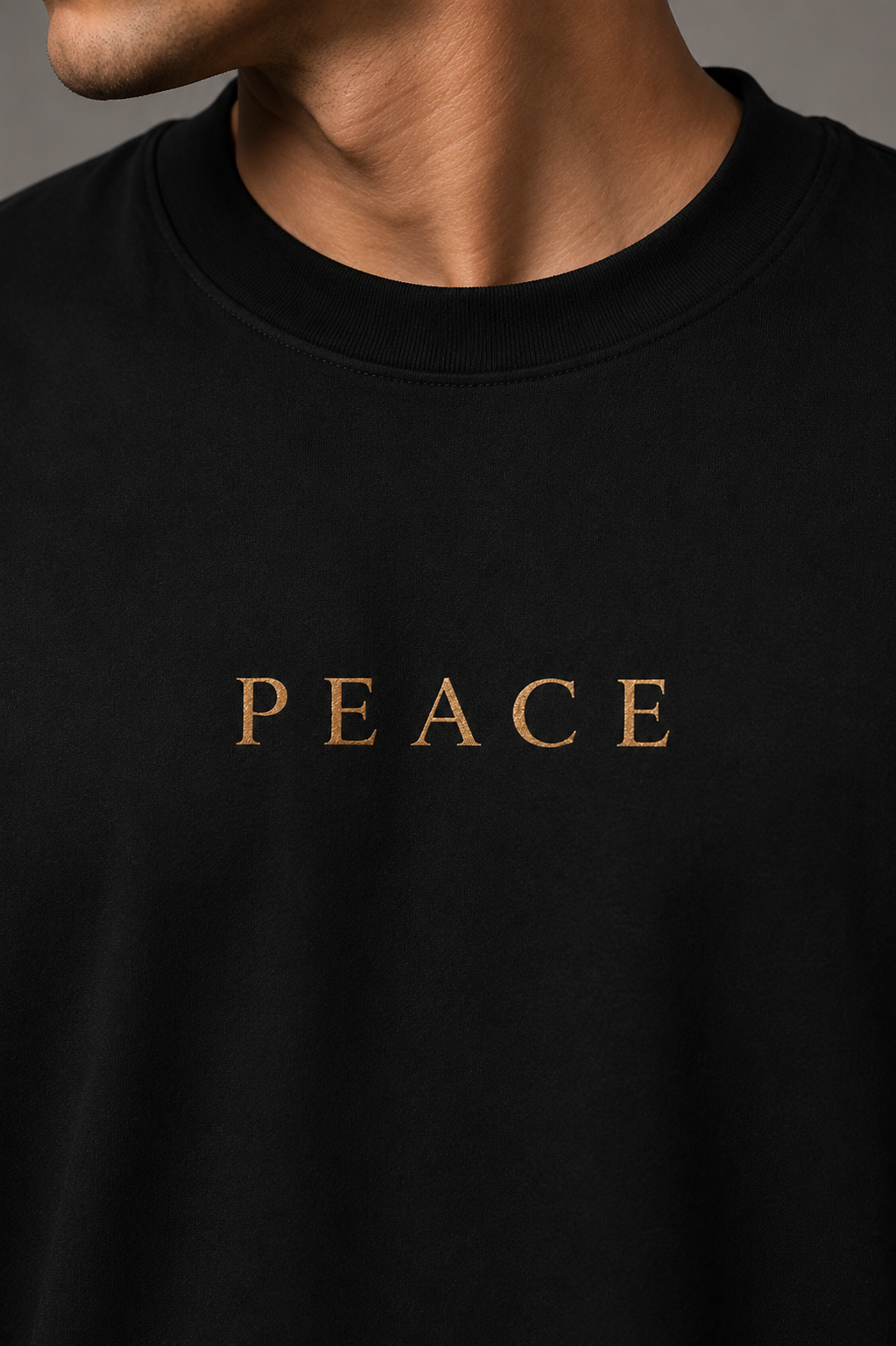 Close-up of a person wearing a black crewneck t-shirt with the word 'PEACE' printed in gold serif letters across the chest.