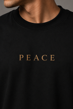 Close-up of a person wearing a black crewneck t-shirt with the word 'PEACE' printed in gold serif letters across the chest.