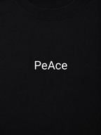 Close-up of a black crewneck t-shirt featuring the word 'PeAce' printed in white sans-serif font across the chest.