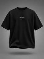 A black short-sleeve crewneck t-shirt with the word 'PeAce' printed in white on the chest, shown against a dark gray gradient background.