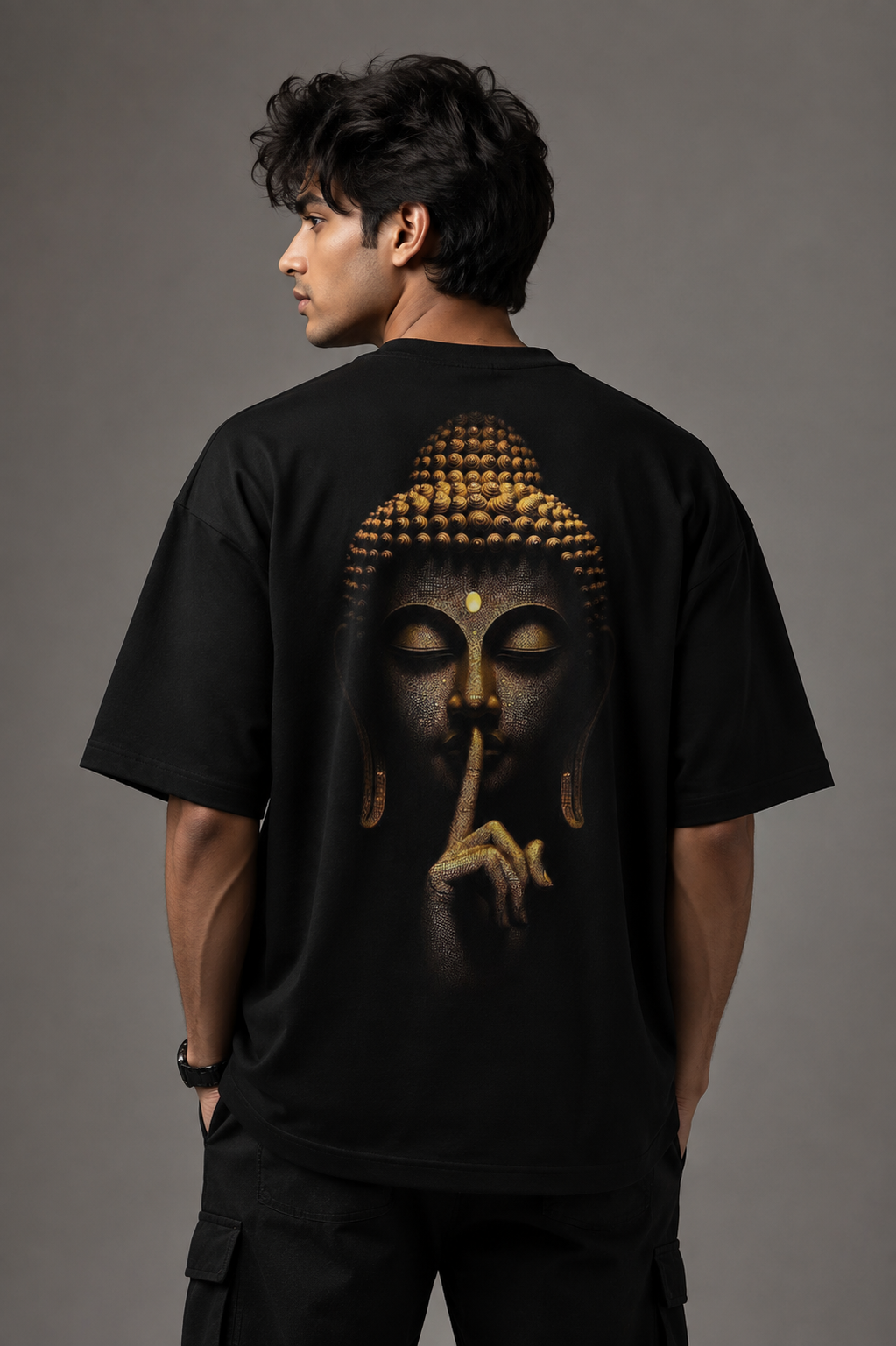 A man shown from the back wearing a black oversized T-shirt with a large graphic print of Buddha's face in gold and dark tones, posed against a solid gray studio background.