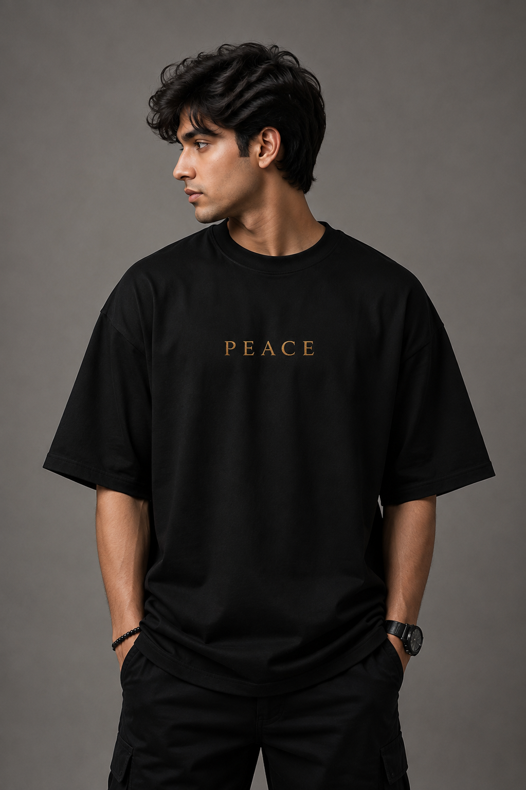 A man wearing a black short-sleeve t-shirt with the word 'PEACE' printed in gold across the chest, posed against a solid dark gray studio background.