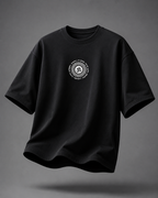 A black short-sleeve crewneck t-shirt with a circular white graphic printed on the center chest, shown floating against a dark gray gradient background.